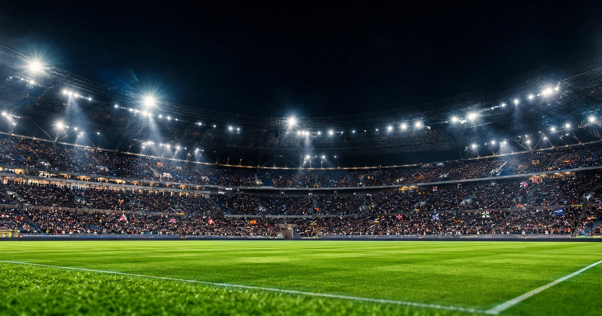 A packed, floodlit football stadium at night, viewed from pitch level with a full crowd in the stands